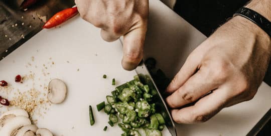 Person slicing green vegetables on a cutting board with mushrooms and chili peppers nearby. - Matrix Sciences