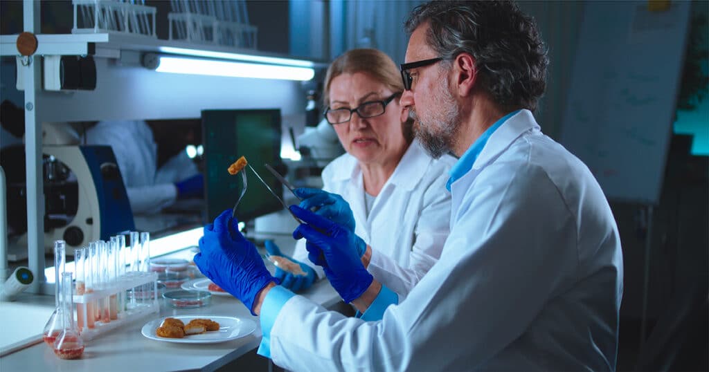 Two scientists in a lab examine a piece of food held between a fork and tweezers. - Matrix Sciences
